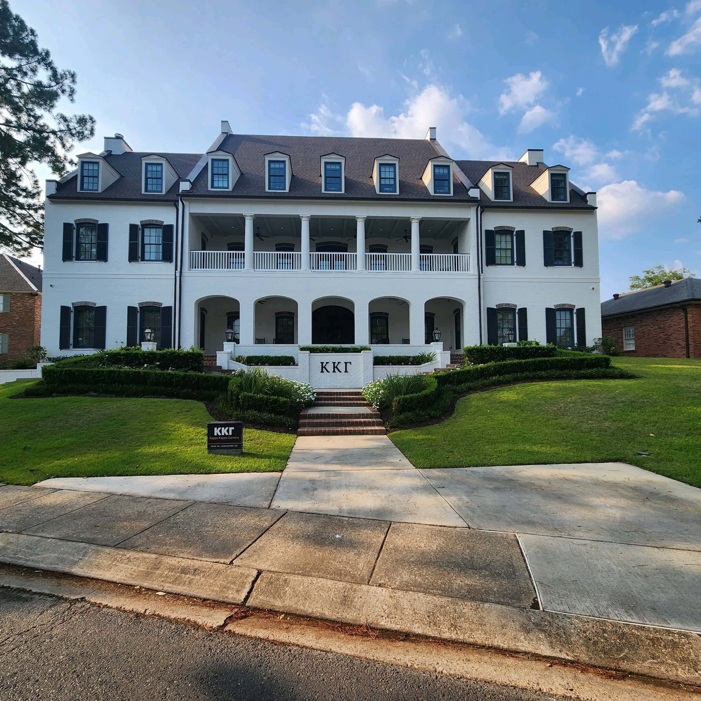 A large, three-story white house with multiple symmetrical windows and a double-decker porch, surrounded by manicured lawns maintained by residential cleaning in Baton Rouge, under a clear blue sky.