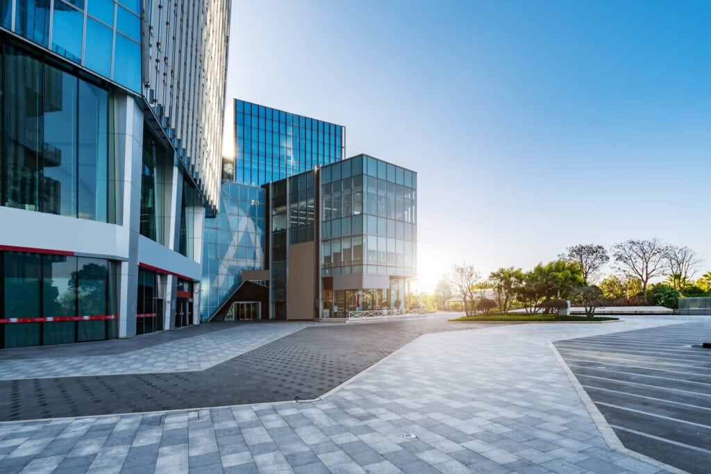 Modern office buildings with reflective glass exteriors in a spacious plaza, illuminated by morning sunlight with a clear blue sky. This serene environment, enhanced by industrial cleaning in Baton Rouge, features trees in the background.