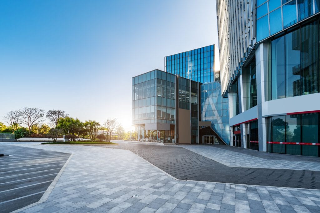 Modern office buildings with reflective glass facades, a paved courtyard, and green spaces, basked in sunlight under a clear blue sky, maintained by janitorial services in Baton Rouge.