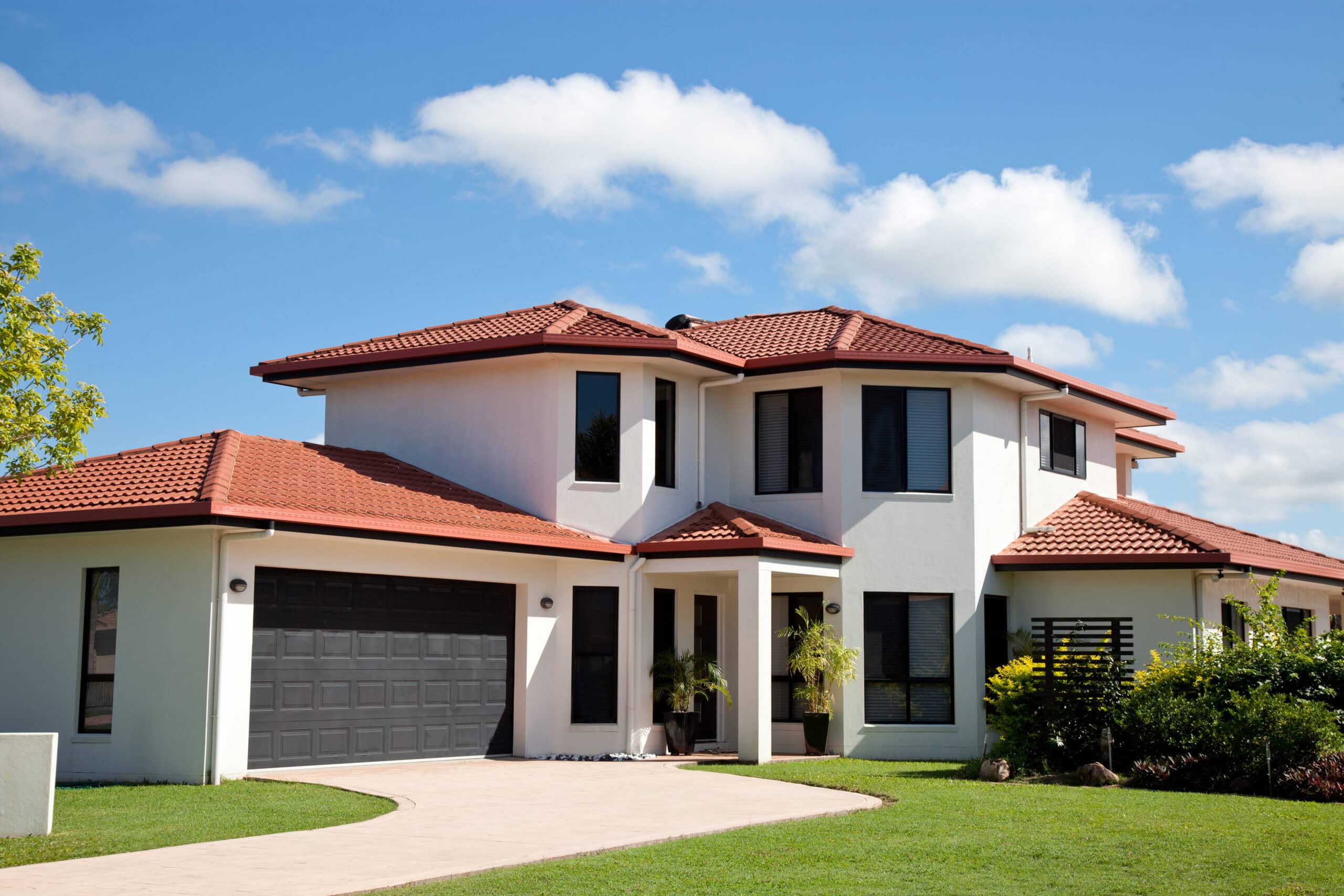 A modern two-story house with a terracotta tile roof, white walls, and an attached garage that receives regular cleaning services in Baton Rouge, set under a blue sky with scattered clouds.