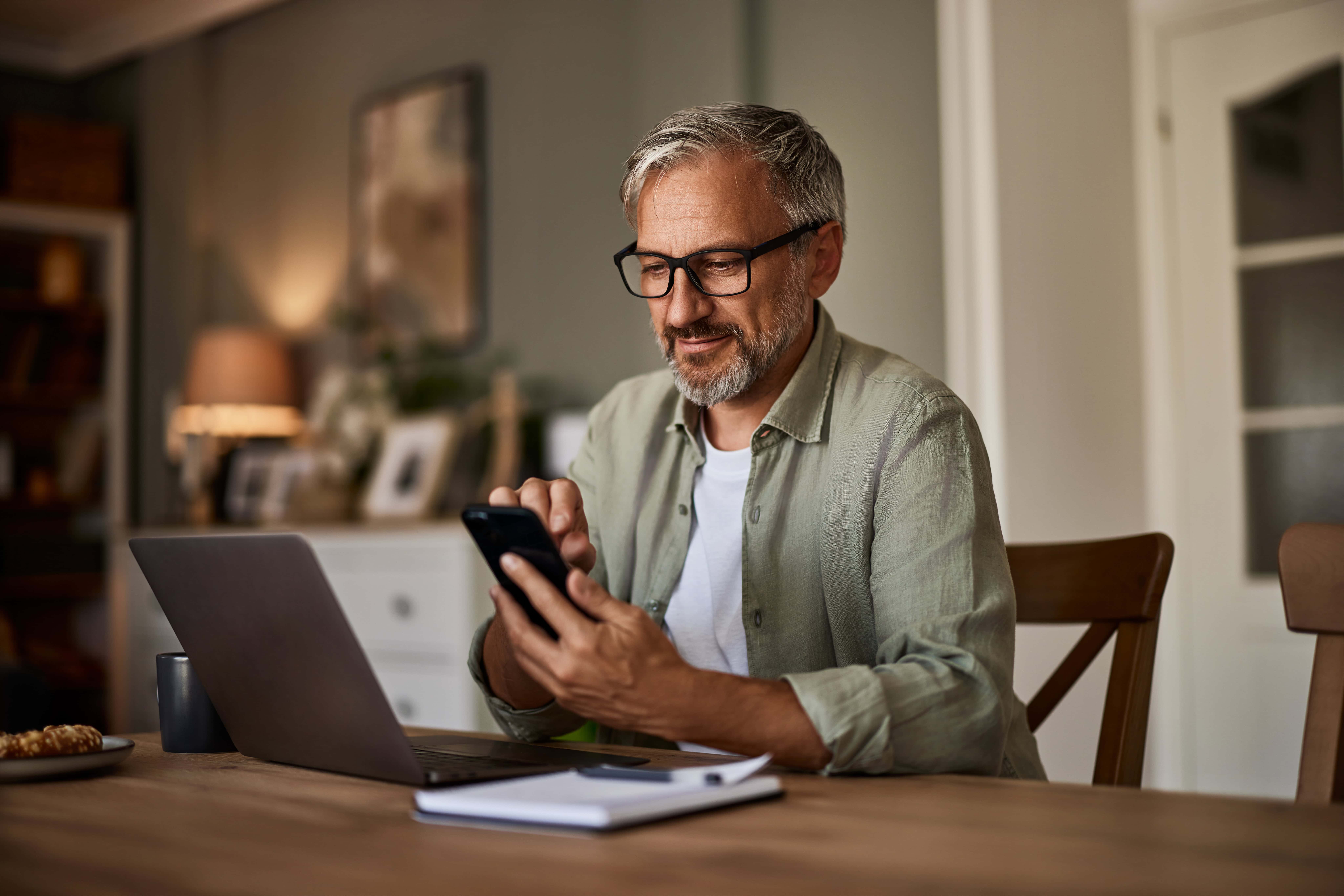 A man sitting at his kitchen table with a laptop and a notepad, preparing to contact HydroClean Solutions for his next cleaning project.