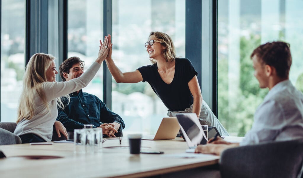 A corporate team high-fiving around a conference table, pleased as to how spotless their office is thanks to top-notch janitorial services