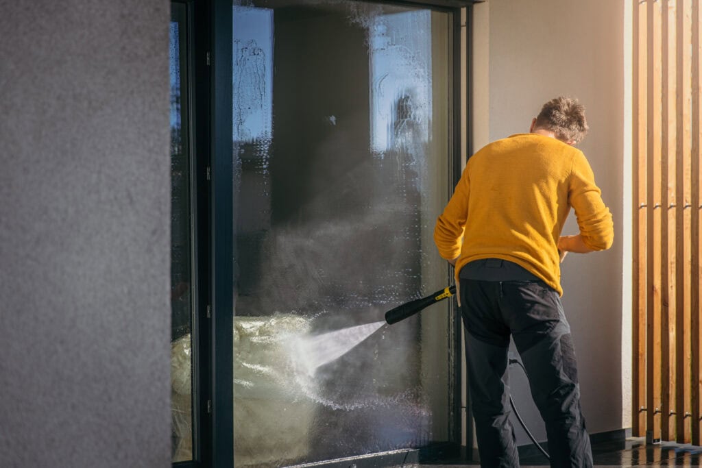 A man in a yellow shirt pressure washing a glass sliding door for a homeowner that needed window cleaning