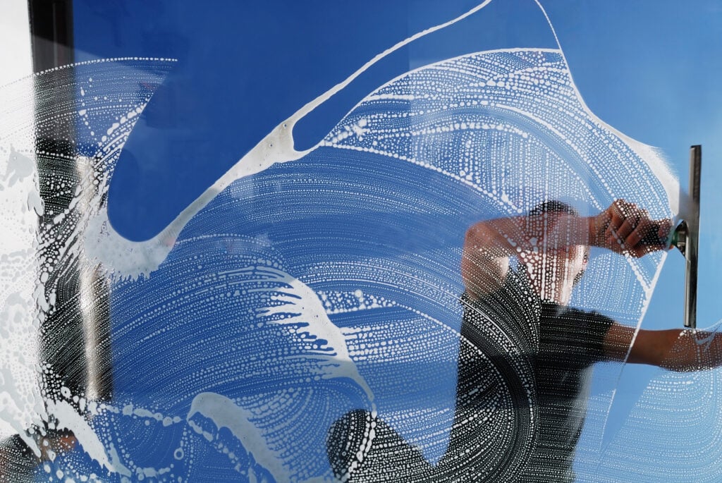 A person using a squeegee for window cleaning in Baton Rouge on a glass window overlaid with a white, swirling digital pattern.